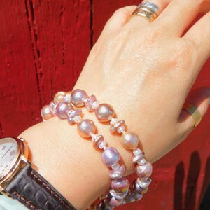 May include: A double strand bracelet made of iridescent pink and white pearls. The bracelet is worn on a person's wrist.