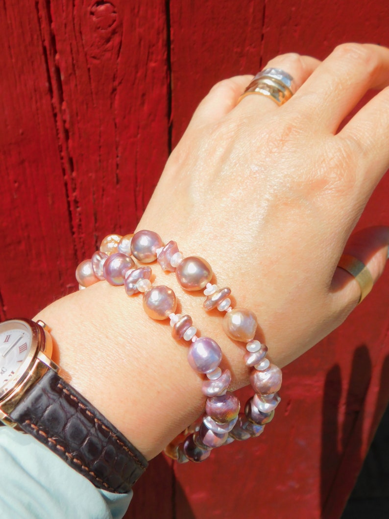 May include: A double strand bracelet made of iridescent pink and white pearls. The bracelet is worn on a person's wrist.