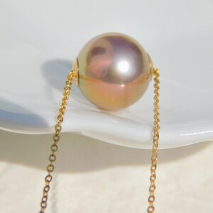 May include: A single, large, iridescent pearl pendant on a delicate gold chain. The pearl has a soft, pearlescent sheen with hints of pink and gold.