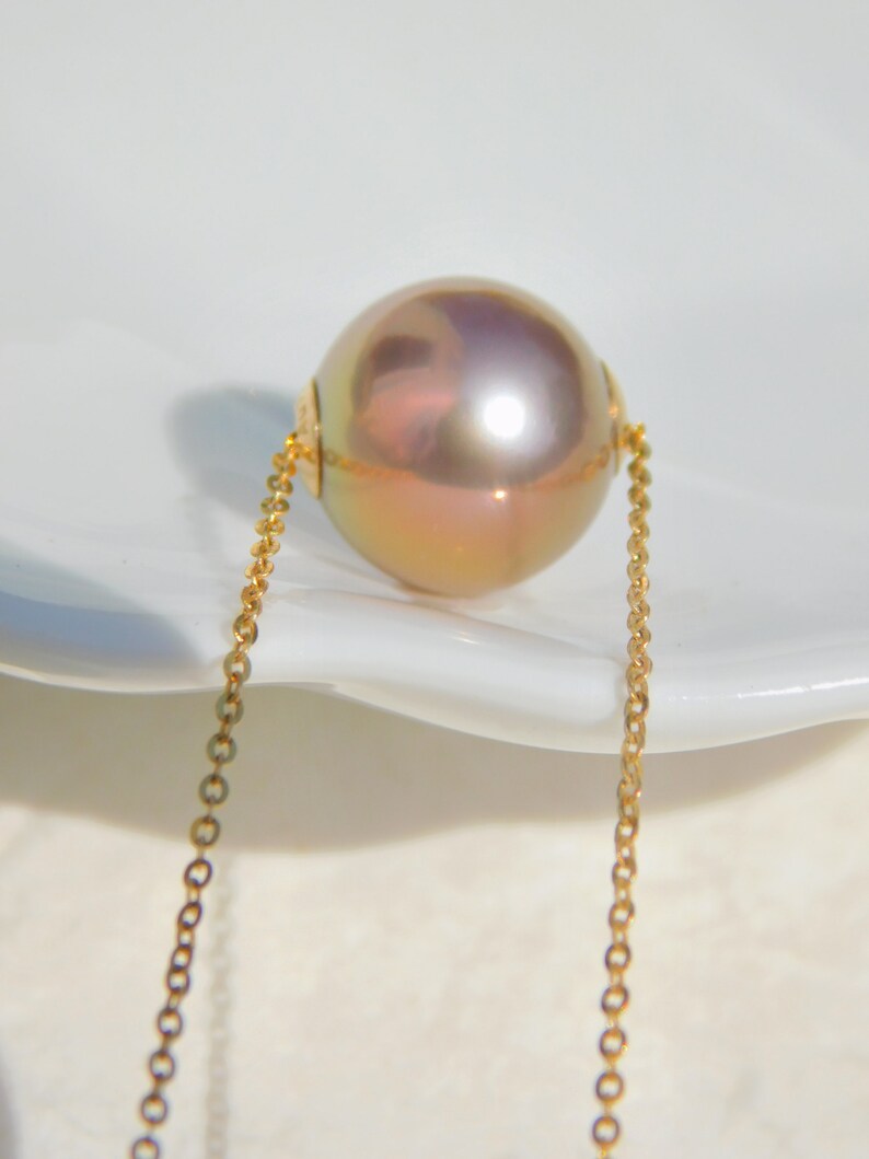 May include: A single, large, iridescent pearl pendant on a delicate gold chain. The pearl has a soft, pearlescent sheen with hints of pink and gold.