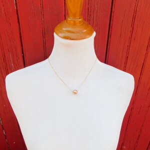 May include: A simple gold chain necklace with a single, round, rose gold pendant.