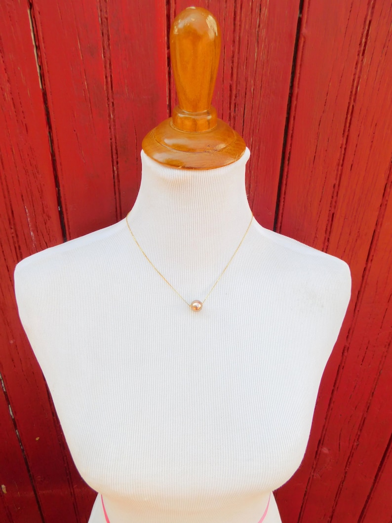 May include: A simple gold chain necklace with a single, round, rose gold pendant.