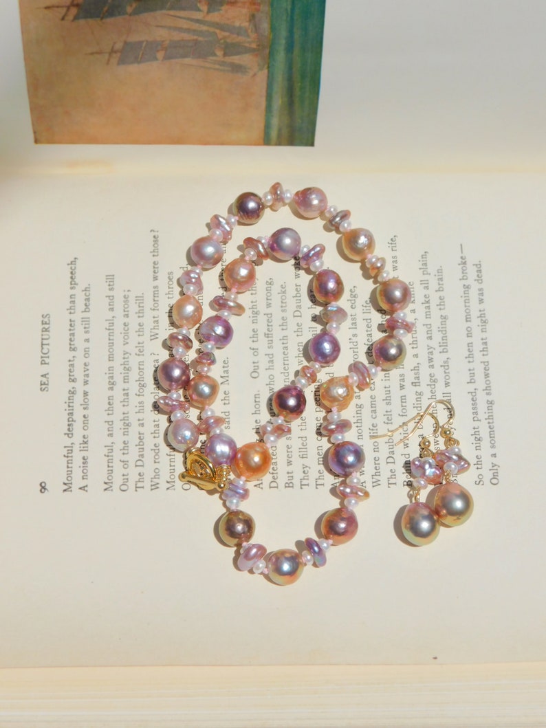 May include: A delicate pearl necklace and earrings set with iridescent pink, purple, and gold tones. The necklace is made of various sizes and shapes of pearls, and the earrings are teardrop shaped.