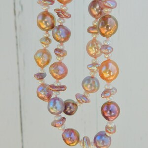 May include: A double strand necklace made of pink and white pearls. The pearls are iridescent and have a soft, natural luster. The necklace is strung on a thin, white cord.