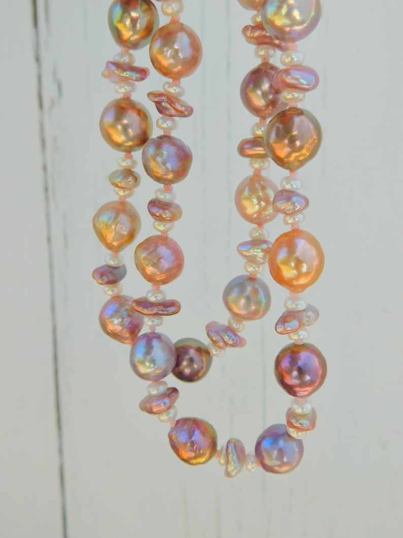 May include: A double strand necklace made of pink and white pearls. The pearls are iridescent and have a soft, natural luster. The necklace is strung on a thin, white cord.