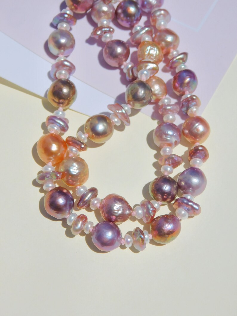 May include: A double strand pearl necklace with pink, white, and peach colored pearls. The pearls are of varying sizes and shapes.