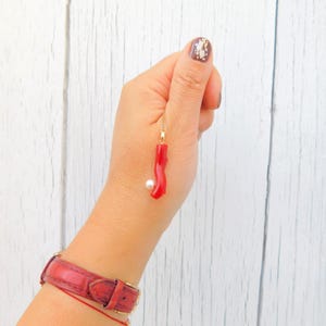 May include: A gold chain necklace with a red coral pendant and a white pearl charm.