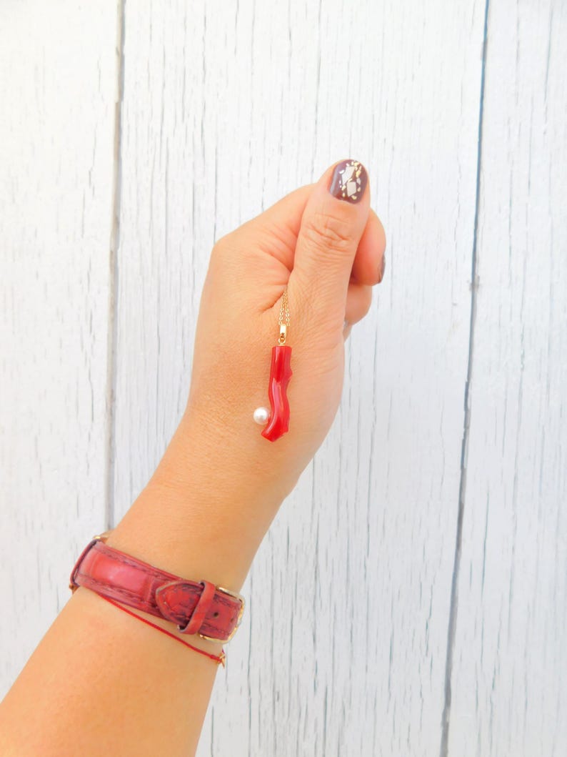 May include: A gold chain necklace with a red coral pendant and a white pearl charm.
