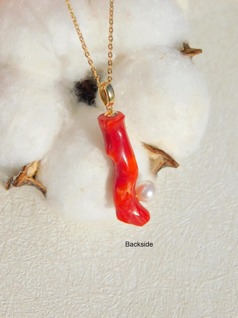 May include: A red coral pendant necklace with a small white pearl accent. The necklace is made of gold chain and the pendant is attached to a gold bail.