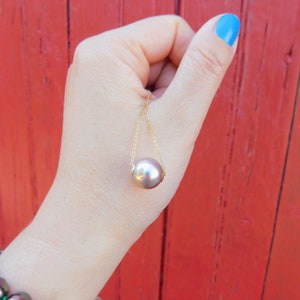 May include: A gold chain necklace with a large, round, iridescent pearl pendant. The pearl is a light brown colour with a hint of pink.