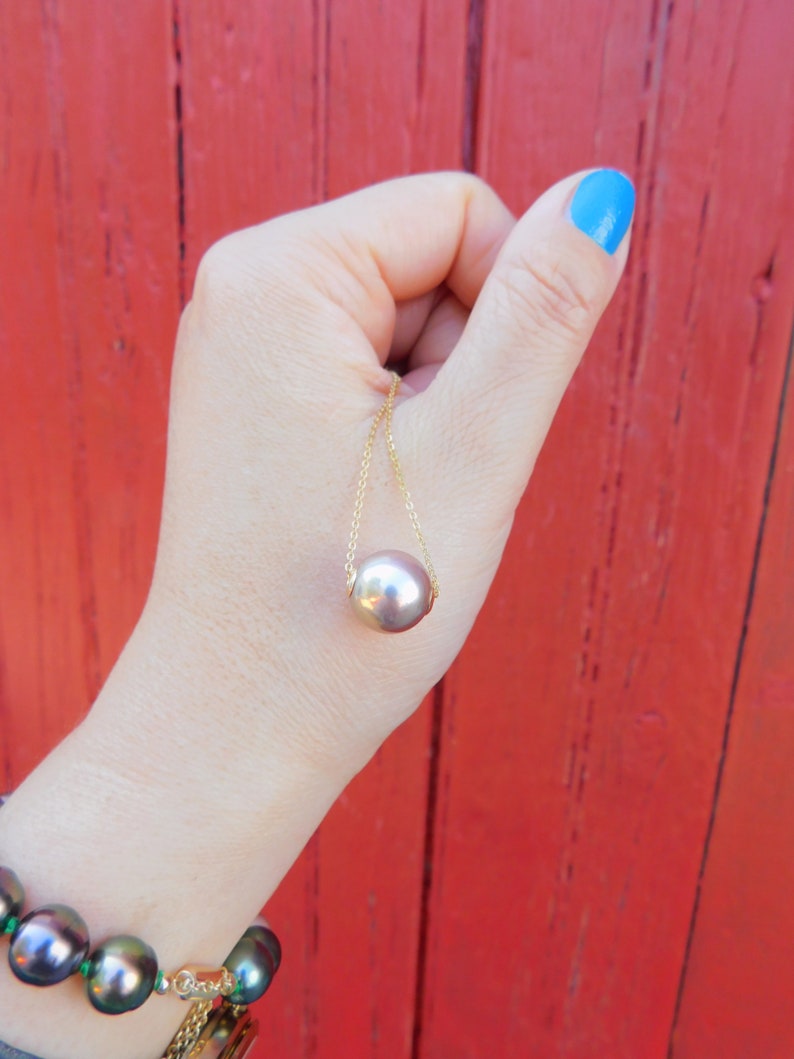 May include: A gold chain necklace with a large, round, iridescent pearl pendant. The pearl is a light brown colour with a hint of pink.