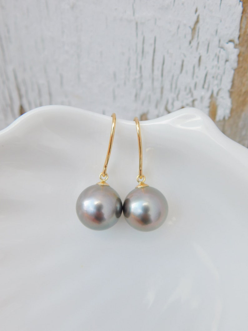 May include: A pair of gray pearl drop earrings with gold hooks. The pearls are round and have a slight iridescent sheen.