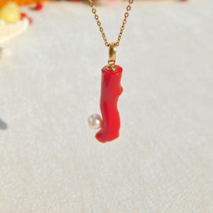 May include: A gold chain necklace with a red coral pendant and a white pearl accent.