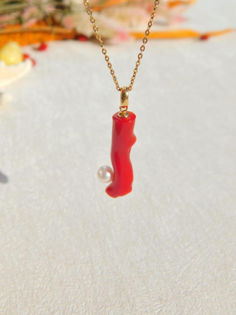 May include: A gold chain necklace with a red coral pendant and a white pearl accent.