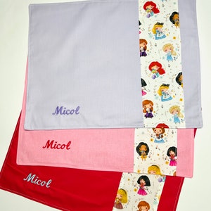 Può includere: Tre tovagliette all'americana a tema principessa. Le tovagliette sono in tonalità di viola, rosa e rosso. Ogni tovaglietta ha un bordo bianco con un motivo di principesse e fiori. Il nome "Micol" è ricamato su ogni tovaglietta.
