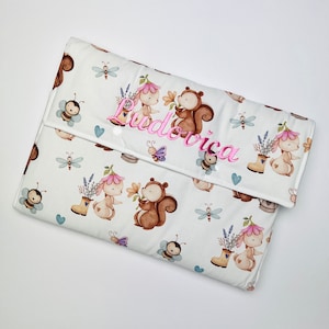 Può includere: Un fasciatoio bianco con un motivo di animali del bosco. Il design include scoiattoli, conigli, api e libellule. Il nome "Ludovica" è ricamato in rosa sul davanti.