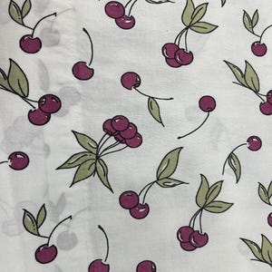 May include: White fabric with a repeating pattern of cherries. The cherries are a deep magenta color, with green leaves and stems. The design is scattered across the fabric.