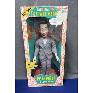 Puede incluir: Muñeco parlante de Pee-wee Herman en su embalaje original. El muñeco viste un traje gris con pajarita roja. La caja presenta el texto "Pee-wee's Playhouse" y "As Seen On TV!"