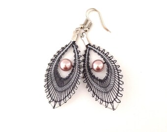 May include: A pair of silver earrings with a delicate black and grey lace design and a single pink pearl in the centre of each earring.