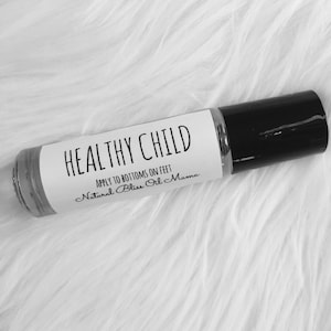May include: A white roller bottle with a black cap. The label reads "HEALTHY CHILD APPLY TO BOTTOMS ON FEET Natural Bliss Oil Mama".