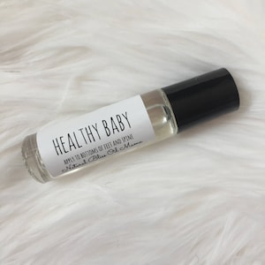 May include: A clear glass roller bottle with a black cap and a white label that reads "HEALTHY BABY APPLY TO BOTTOMS OF FEET AND SPINE Natural Bliss Oil Mama".