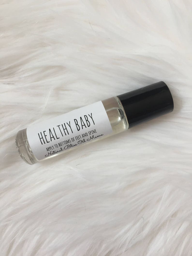 May include: A clear glass roller bottle with a black cap and a white label that reads "HEALTHY BABY APPLY TO BOTTOMS OF FEET AND SPINE Natural Bliss Oil Mama".