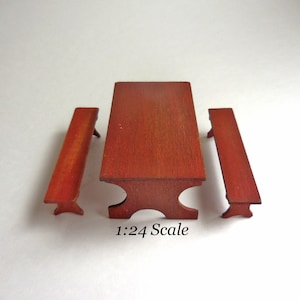 May include: A miniature wooden table and two benches set. The table and benches are a deep red color and have a rustic finish. The set is 1:24 scale.