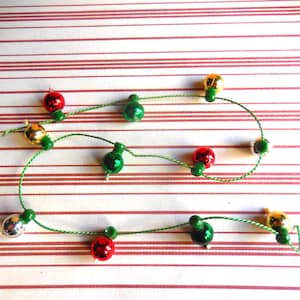 Puede incluir: Una cadena de luces navideñas con adornos rojos, verdes y dorados. Las luces están enhebradas en un cordón verde y están colgadas sobre un fondo a rayas rojo y blanco.