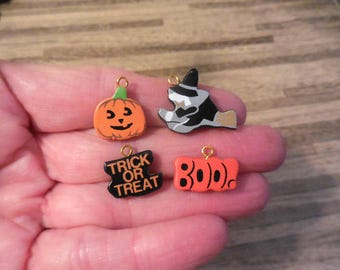 May include: Four Halloween-themed charms with gold-coloured jump rings. The charms are made of wood and painted in orange, black, and white. The charms depict a pumpkin, a witch, a "Trick or Treat" sign, and the word "BOO".