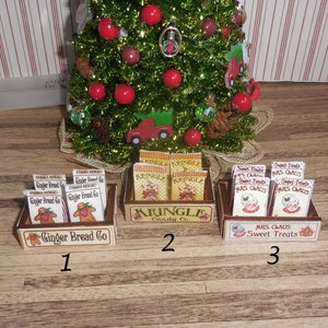 May include: Three wooden crates filled with miniature packages of gingerbread, candy, and sweet treats. The crates are labeled "Ginger Bread Co", "Kringle Candy Co", and "Mrs. Claus Sweet Treats".