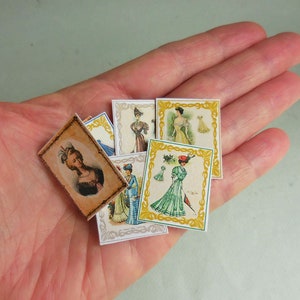 May include: A collection of six vintage-style cards featuring women in various dresses. The cards are decorated with gold and white borders and have a slightly aged look.
