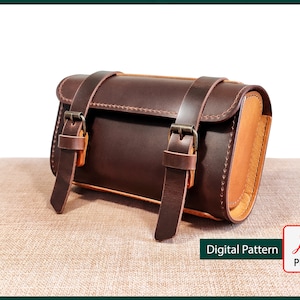 Op de afbeelding: Een bruine leren zadeltas met twee gespen en een tan lederen afwerking. De tas ligt op een bruine stoffen ondergrond. Digitaal patroon PDF.