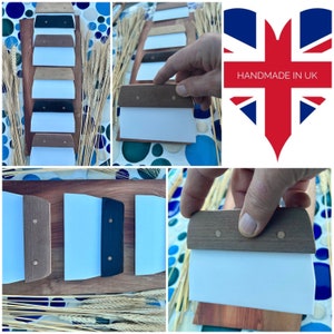 May include: A selection of dough scrapers with wooden handles and white blades. The handles are in various colours, including dark brown, light brown, and black. The scrapers are presented on a wooden board with wheat.