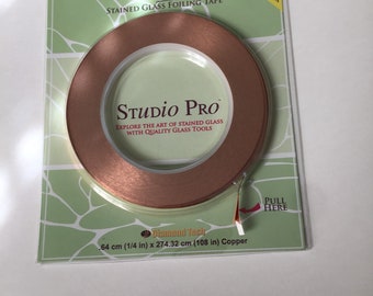 Może przedstawiać: Rolka miedzianej taśmy do szkła witrażowego w przezroczystym plastikowym opakowaniu. Opakowanie zawiera napis "Studio Pro" i "Easy Pull Dispenser Pack". Taśma ma wymiary 0,64 cm x 274,32 cm.