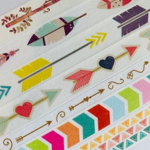 May include: A set of colorful washi tapes with various designs, including arrows, feathers, hearts, and geometric patterns. The tapes are on a white background.