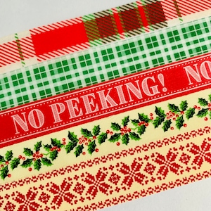 May include: Four rolls of washi tape with a Christmas theme. The top roll has a red and green plaid pattern. The second roll has a green and white plaid pattern. The third roll has a red background with the text "NO PEEKING!" in white. The bottom roll has a yellow background with a green holly pattern and a red and white snowflake pattern.