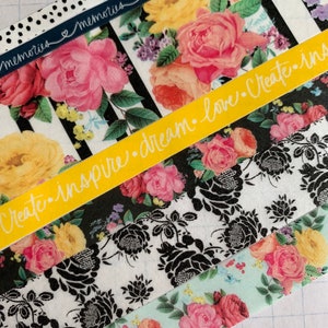 May include: Five rolls of washi tape with floral patterns. The top roll has black and white polka dots with the text "memories" in navy blue. The second roll has black and white stripes with a yellow floral pattern. The third roll has a yellow background with the text "create. inspire. dream. love. create. share" in white. The fourth roll has a black and white floral pattern. The fifth roll has a light blue background with a pink and yellow floral pattern.