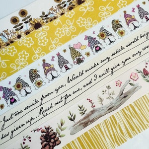 May include: Five rolls of washi tape featuring a variety of designs, including gnomes, sunflowers, and floral patterns. The tape is yellow, white, and brown. The text on the tape reads "Just one smile from you, Would make my whole world bright".