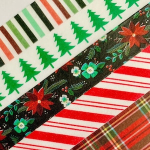 May include: Five rolls of washi tape with Christmas themes. The tapes feature a red and white striped pattern, a plaid pattern, a floral pattern with red flowers, a pattern of green Christmas trees, and a green, brown, and red striped pattern.