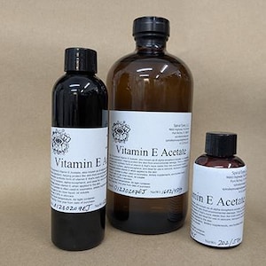 May include: Three bottles of Vitamin E products. The bottles are different sizes and have black caps and white labels with black text. The largest bottle is amber-colored, while the other two are dark.