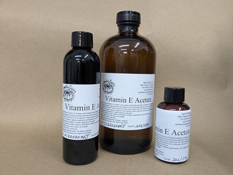 Puede incluir: Tres botellas de productos de vitamina E. Las botellas son de diferentes tama&ntilde;os y tienen tapas negras y etiquetas blancas con texto negro. La botella m&aacute;s grande es de color &aacute;mbar, mientras que las otras dos son oscuras.
