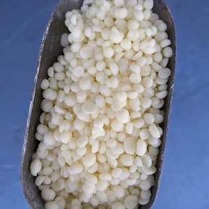 May include: A scoop filled with white, round, wax beads.