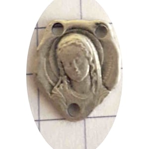 Può includere: Ciondolo in metallo argentato con un'immagine in rilievo della Vergine Maria. Il ciondolo ha tre fori per attaccarlo a una collana o un braccialetto.