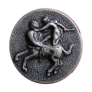 Può includere: Bottone rotondo argentato con un rilievo dettagliato di un centauro e una figura umana. Le figure sono impegnate in una lotta, con la figura umana che sembra essere sulla schiena del centauro. Il bottone ha uno sfondo strutturato e un bordo rosso.
