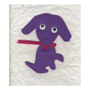 May include: Purple felt dog with pink felt collar and a pink felt flower. The dog has white googly eyes and is stitched with pink thread.