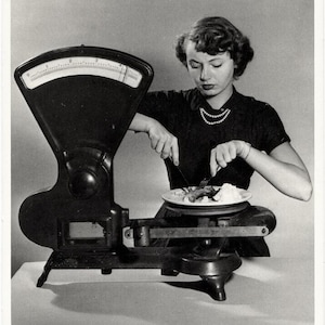 Carte vintage, une femme déjeunant directement sur une balance, datée 1950, édition américaine, collection, humour, régime alimentaire