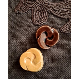 Peut inclure: Deux boutons en céramique avec un motif de nœud. Un bouton est brun et l'autre est de couleur jaune clair.
