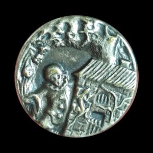 May include: An antique silver-coloured button with a detailed relief design. The button depicts a costumed figure, a building, and foliage. The design is set against a dark background, highlighting the intricate details of the button's surface.