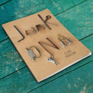 Puede incluir: Un libro marrón con la palabra "Junk DNA" escrita en negro en la portada. Las letras están hechas de varios objetos metálicos, incluyendo una llave, una llave inglesa, un tornillo y un clavo. El nombre del autor, "Clare Thompson", está impreso en negro debajo del título.