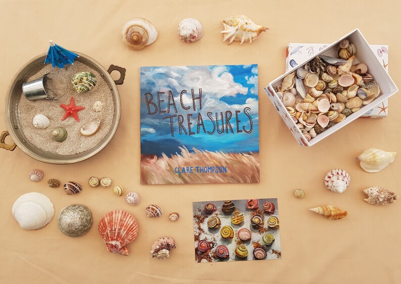 May include: A flat lay of seashells, a book titled "Beach Treasures" by Clare Thompson, and a small box filled with seashells. The book cover features a painting of a blue sky with white clouds and tall grass.